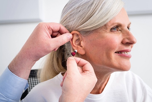 Eine ältere Frau bekommt ein Hörgerät eingesetzt, Hörgeräteanpassung für Senioren.